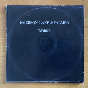 May include: Black vinyl record album cover with white text that reads "Emerson Lake & Palmer" and "Works". A stylized "ELP" logo is centred on the cover.