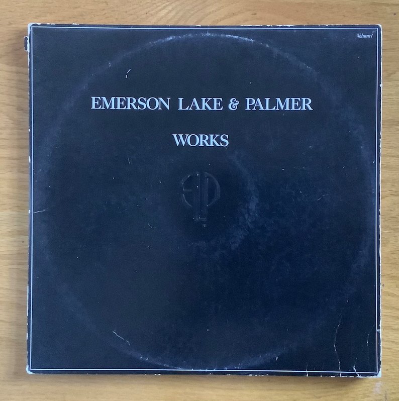 May include: Black vinyl record album cover with white text that reads "Emerson Lake & Palmer" and "Works". A stylized "ELP" logo is centred on the cover.