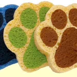 Op de afbeelding: Drie gele sponzen in de vorm van poot afdrukken. De poot afdrukken zijn omrand met blauw, groen en bruin.