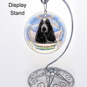 Peut inclure: Une décoration ronde blanche avec un chien Cocker Spaniel noir et blanc avec des ailes d'ange. La décoration a un arc-en-ciel et des nuages en arrière-plan. Le texte "I Crossed the Rainbow Bridge Knowing that I Was Loved" est imprimé sur la décoration.