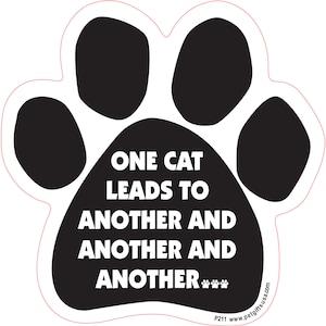 以下が含まれることがあります： 白い背景に「One cat leads to another and another and another... 」という白い文字が書かれた黒い肉球のプリント。肉球は、下部にウェブサイトのアドレスが書かれたステッカーです。