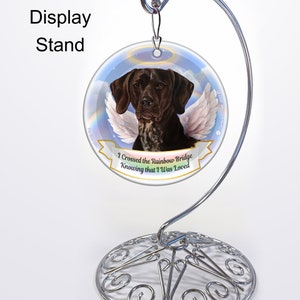 May include: A round glass ornament with a brown and white German Shorthaired Pointer dog with angel wings. The ornament has a blue sky background with a rainbow and clouds. The text "I Crossed the Rainbow Bridge Knowing that I Was Loved" is printed on a white banner.
