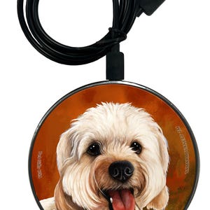 Könnte beinhalten: Runder, kabelloser Ladegerät mit einem hellen Hund. Es hat ein schwarzes Kabel und einen USB-Anschluss. Der Text "TAMARA BURNETT TM" steht unten. Zum Aufladen von Smartphones.