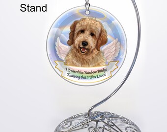 May include: A round ornament featuring a golden doodle dog with angel wings and a halo, displayed on a silver metal ornament stand. The ornament has the text "I Crossed the Rainbow Bridge Knowing that I Was Loved".