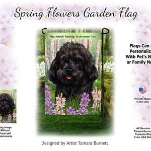 Puede incluir: Una bandera de jardín negra con un perro negro con patas blancas y una nariz rosa. El perro está sentado en un campo de flores moradas y rosas. La bandera tiene el texto "The Smith Family Welcomes You". La bandera está diseñada por la artista Tamara Burnett.