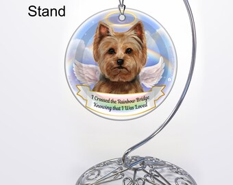 May include: A round, white ceramic ornament with a picture of a Yorkshire Terrier with angel wings. The ornament has a rainbow bridge and the text "I crossed the rainbow bridge knowing that I was loved". The ornament is on a silver metal display stand.