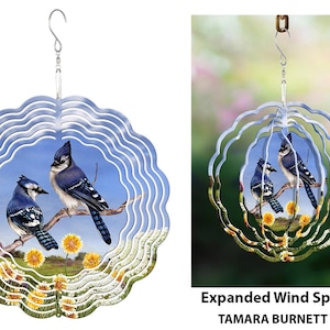 May include: A decorative wind spinner featuring two blue jays perched on a branch, set against a blue sky and yellow flowers. The spinner has a layered, wavy design and a silver hanging hook.