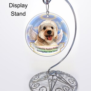 Könnte beinhalten: Runder Gedenk-Ornament für Hunde mit Engelsflügeln und Heiligenschein, präsentiert auf einem silbernen Metallständer. Das Ornament zeigt einen lächelnden Hund mit dem Text "I Crossed the Rainbow Bridge Knowing that I Was Loved."