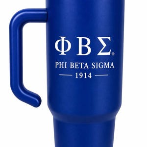 May include: A royal blue insulated tumbler with a handle, a clear lid, and a matching blue straw. The front features the white Greek letters ΦΒΣ, the text PHI BETA SIGMA, and the year 1914 printed in a clean, centered font on the smooth surface.