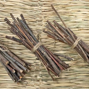May include: Three bundles of small, brown wooden sticks tied with twine, arranged on a textured, light brown surface. The sticks vary in color from light tan to dark brown.