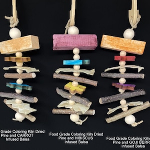 Puede incluir: Tres juguetes coloridos para pájaros colgados sobre un fondo negro. Cada juguete está hecho de madera, con varias formas y colores, incluyendo naranja, rosa, rojo, azul y verde. El texto se encuentra en la parte inferior.