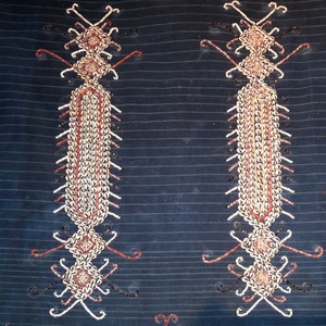 May include: Two symmetrical designs on a dark blue fabric, each made of small white and brown shells arranged in a geometric pattern.