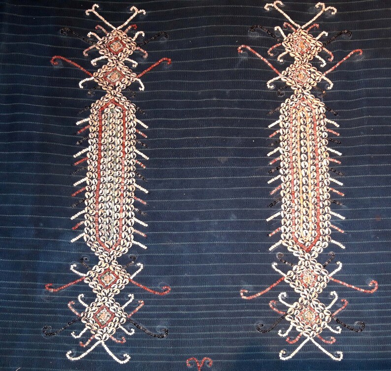 May include: Two symmetrical designs on a dark blue fabric, each made of small white and brown shells arranged in a geometric pattern.