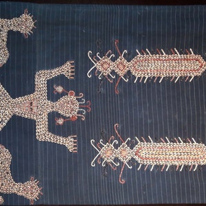 May include: A dark blue textile with embroidered figures and designs in white, red, and gold thread. The figures are stylized human figures with outstretched arms and legs. The designs are geometric patterns.