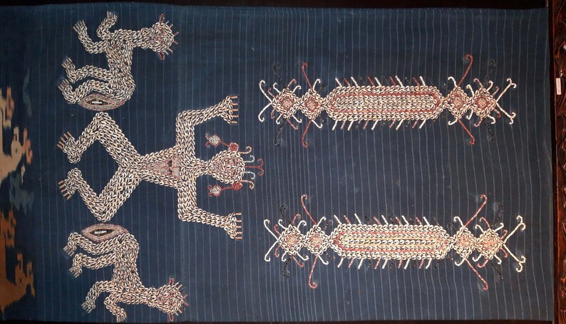 May include: A dark blue textile with embroidered figures and designs in white, red, and gold thread. The figures are stylized human figures with outstretched arms and legs. The designs are geometric patterns.