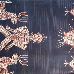 May include: A dark blue textile with a repeating pattern of embroidered figures and geometric shapes. The figures are white and have a stylized human form with a crown on their head. The geometric shapes are white with a diamond shape in the center.