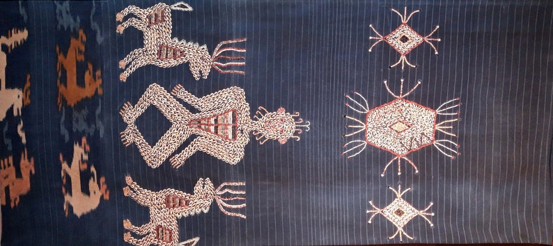 May include: A dark blue textile with a repeating pattern of embroidered figures and geometric shapes. The figures are white and have a stylized human form with a crown on their head. The geometric shapes are white with a diamond shape in the center.
