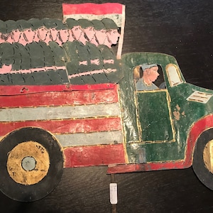 Puede incluir: Un camión de juguete de hojalata vintage pintado en rojo, blanco y verde con un conductor en la cabina y una fila de soldados en la parte trasera. El camión tiene una bandera en la parte trasera.