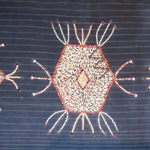 May include: A dark blue fabric with three decorative designs made of white, brown, and red beads. The designs are a hexagon in the center and two diamonds on either side.