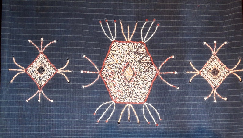 May include: A dark blue fabric with three decorative designs made of white, brown, and red beads. The designs are a hexagon in the center and two diamonds on either side.