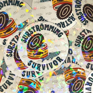 May include: A close-up of several round stickers with a holographic finish. The stickers feature a stylized illustration of a can of fermented herring, with the text "SURSTRÖMMING" and "SURVIVOR" printed on the stickers.