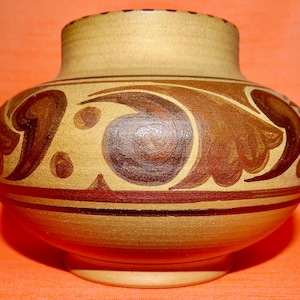 May include: A brown ceramic vase with a decorative design of brown swirls and dots. The vase has a rounded body and a wide opening.