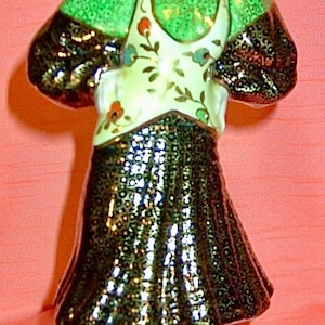 May include: A porcelain figurine of a woman wearing a green and gold dress with a floral pattern. She has red hair and is standing on a brown base.