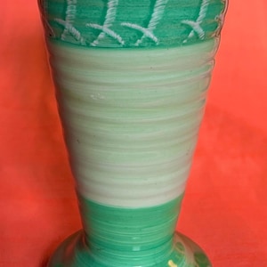 May include: A tall, decorative vase with a flared top and a rounded base. The vase features a color scheme of green and white, with a textured design around the top and base. The vase is approximately 10 inches tall.