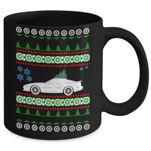 May include: Black ceramic mug with a festive design. The mug features a white car with a Christmas tree on top, snowflakes, and a pattern of green trees, red circles, and white circles. The mug has a black handle.