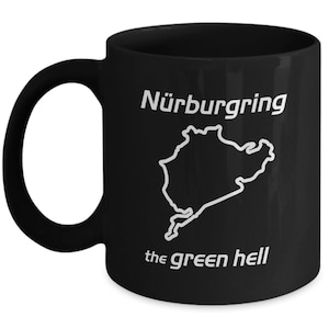 Puede incluir: Taza de café de cerámica negra con un contorno blanco del circuito de carreras de Nürburgring y el texto "Nürburgring the green hell".