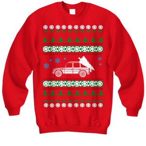 May include: Red Christmas sweater with a white car carrying a Christmas tree. The sweater has a green and white snowflake pattern.
