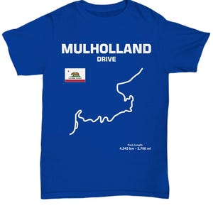 以下が含まれることがあります： ロイヤルブルーのTシャツに、Mulholland Driveのロードコースの白いアウトラインが描かれています。Tシャツには「Mulholland Drive」の文字と、クマが描かれたカリフォルニア州の旗もデザインされています。