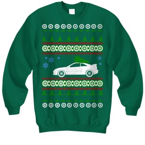 Könnte beinhalten: Grüner Weihnachtspullover mit einem weißen Auto und einem Weihnachtsbaum darauf. Der Pullover hat ein sich wiederholendes Muster aus Schneeflocken, Kreisen und Dreiecken.