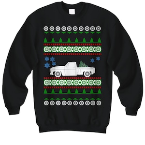 Puede incluir: Suéter navideño negro con una camioneta blanca que lleva un árbol de Navidad. El suéter tiene un patrón de copo de nieve verde, rojo y blanco.