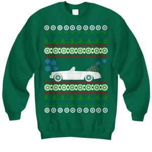 May include: Green sweatshirt with a white convertible car carrying a Christmas tree. The sweater has a festive pattern of snowflakes, trees, and circular designs in white, red, and green. A holiday-themed apparel item.