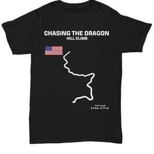 May include: Black t-shirt with white text that reads "Chasing the Dragon Hill Climb". A small American flag is in the upper left corner. A white outline of a winding road is in the center of the shirt. The text "Track Length: 3.5 km - 2.17 mi" is in the bottom right corner.