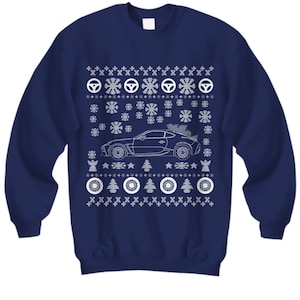 May include: A navy blue sweatshirt with a white Christmas-themed design featuring a car with a Christmas tree on top. The design includes snowflakes, stars, and tire tracks.