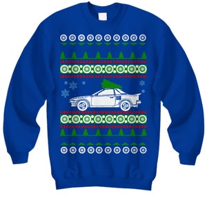 May include: A blue Christmas sweater with a white car carrying a Christmas tree on top. The sweater has a red and green snowflake pattern.