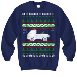 Peut inclure: Un pull de Noël bleu marine avec une silhouette blanche d'un camion de ramassage transportant un sapin de Noël. Le pull a un motif rouge et vert avec des flocons de neige et des cercles.