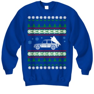 May include: A blue Christmas sweater with a white car carrying a Christmas tree. The sweater has a repeating pattern of snowflakes, Christmas trees, and tire tracks.