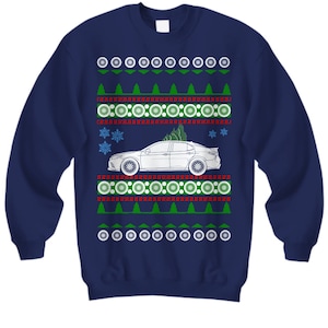 May include: A navy blue Christmas sweater with a white car and a Christmas tree on top. The sweater has a red and green snowflake pattern.