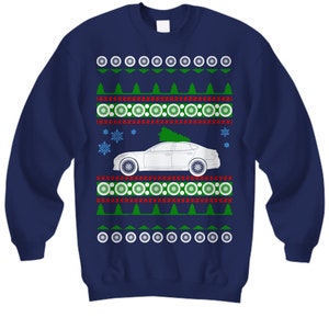 May include: A navy blue Christmas sweater with a white car carrying a Christmas tree on top. The sweater has a red and green snowflake pattern.