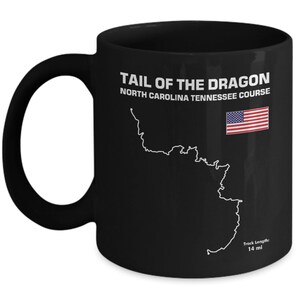 May include: Black ceramic mug with a white graphic of the Tail of the Dragon motorcycle road in North Carolina and Tennessee. The graphic includes the text "Tail of the Dragon North Carolina Tennessee Course" and "Track Length: 14 mi". An American flag is also included in the graphic.