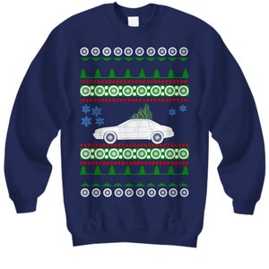 May include: A navy blue Christmas sweater with a white car carrying a Christmas tree. The sweater has a repeating pattern of green trees, red and white circles, and snowflakes.