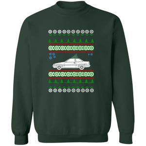 May include: Dark green sweatshirt with a white car graphic carrying a Christmas tree. The design includes repeating patterns of green trees, red lines, and white circles, creating a festive, holiday-themed look.