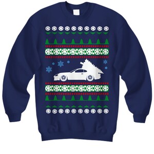 May include: A navy blue Christmas jumper featuring a white silhouette of a car with a Christmas tree on top. The jumper has a red and green snowflake pattern.