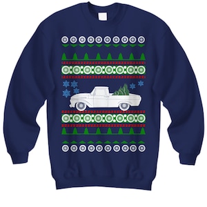 May include: A navy blue sweatshirt featuring a white pickup truck carrying a Christmas tree. The truck is surrounded by a festive pattern of red and green snowflakes, circles, and trees.