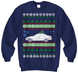 May include: Navy blue sweatshirt with a festive design. The design includes a white car with a Christmas tree on top, surrounded by green trees, snowflakes, and circular patterns. The sweatshirt is a crew neck.