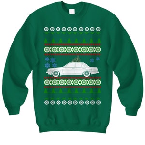 May include: A green Christmas sweater with a white car and a Christmas tree on it. The sweater has a white, red, and green pattern.