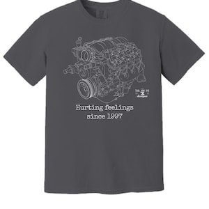 Puede incluir: Una camiseta gris oscuro con un contorno blanco de un motor de coche y el texto "Hurting feelings since 1997" y "Tool and Dye Designs".